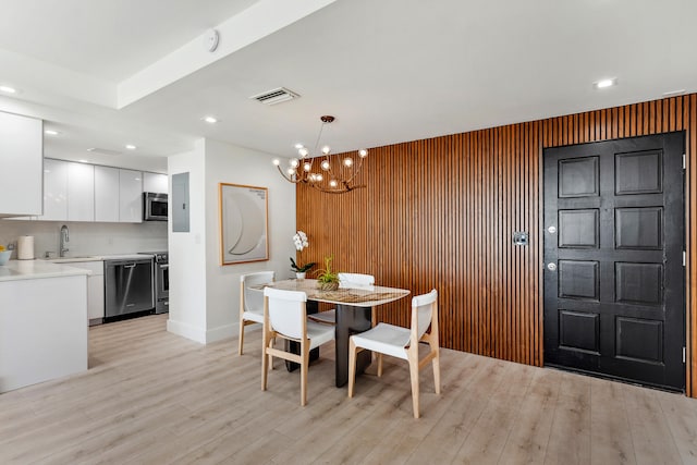 dining area with an inviting chandelier, sink, light wood-type flooring, and wooden walls