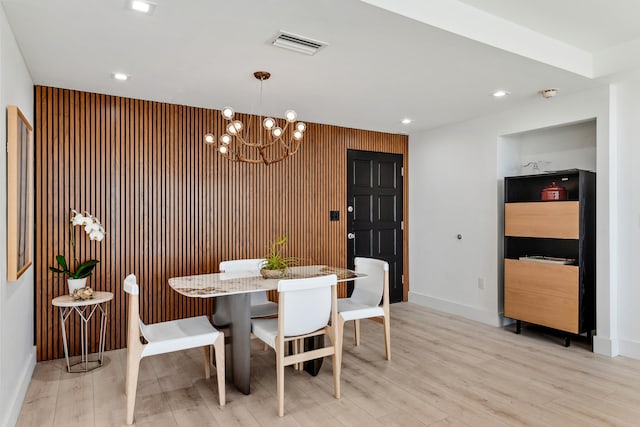 dining area featuring a notable chandelier, light wood-type flooring, and wood walls