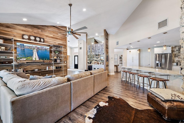 living room with ceiling fan, high vaulted ceiling, wood-type flooring, and wooden walls