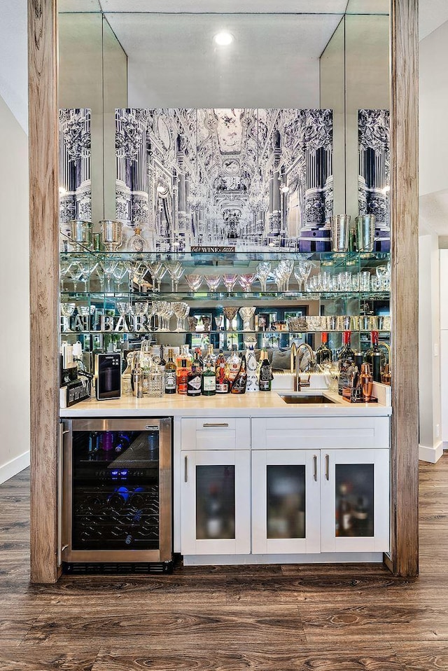 bar with a bar, a sink, wood finished floors, and beverage cooler