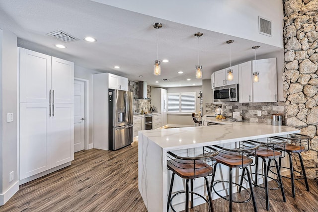 kitchen featuring hanging light fixtures, kitchen peninsula, white cabinetry, appliances with stainless steel finishes, and tasteful backsplash