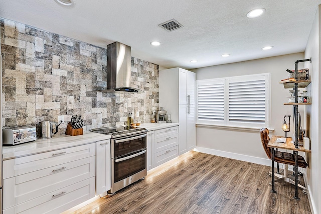 kitchen featuring visible vents, wood finished floors, wall chimney exhaust hood, tasteful backsplash, and double oven range