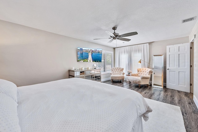 bedroom featuring a textured ceiling, a ceiling fan, baseboards, dark wood-type flooring, and visible vents