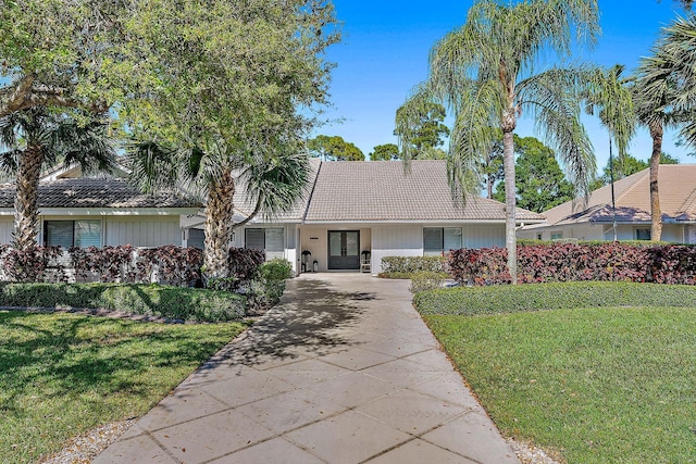 view of front facade featuring concrete driveway, french doors, a tile roof, and a front yard