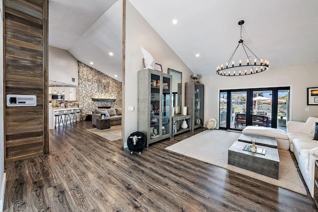 living area with high vaulted ceiling, a chandelier, a stone fireplace, and wood finished floors
