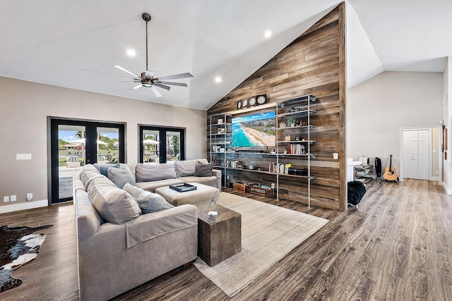 living room featuring french doors, hardwood / wood-style flooring, ceiling fan, high vaulted ceiling, and wood walls