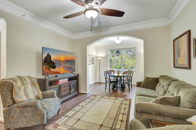 living room featuring arched walkways, crown molding, ceiling fan, wood finished floors, and baseboards