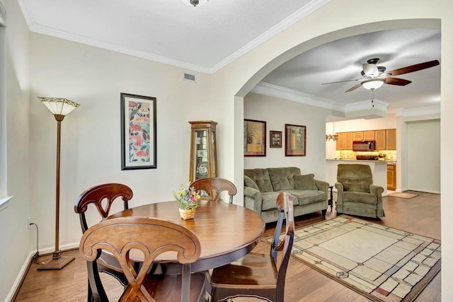 dining area featuring arched walkways, visible vents, light wood-style floors, ornamental molding, and a ceiling fan