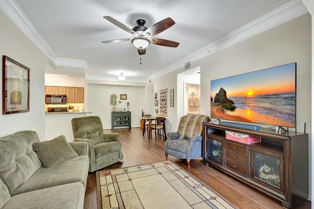 living area featuring a textured ceiling, wood finished floors, visible vents, a ceiling fan, and ornamental molding