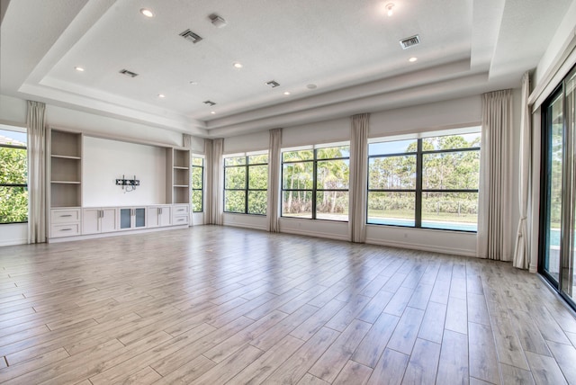 unfurnished living room featuring light hardwood / wood-style floors, a textured ceiling, a raised ceiling, and built in shelves