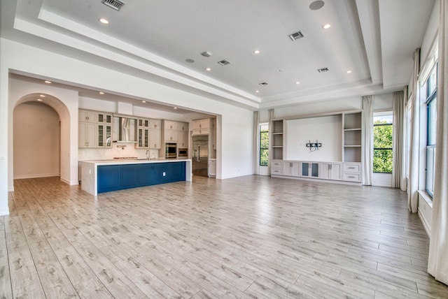 unfurnished living room with plenty of natural light, a raised ceiling, and light wood-type flooring