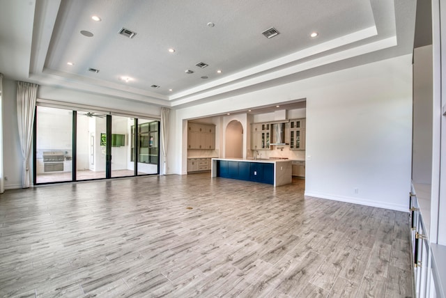 unfurnished living room with a textured ceiling, a raised ceiling, and light hardwood / wood-style flooring