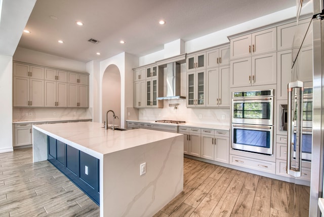 kitchen featuring a center island with sink, sink, appliances with stainless steel finishes, light stone countertops, and light hardwood / wood-style flooring