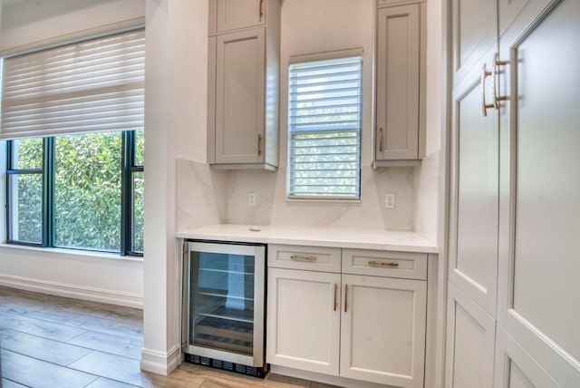 bar featuring white cabinetry, beverage cooler, and light hardwood / wood-style flooring