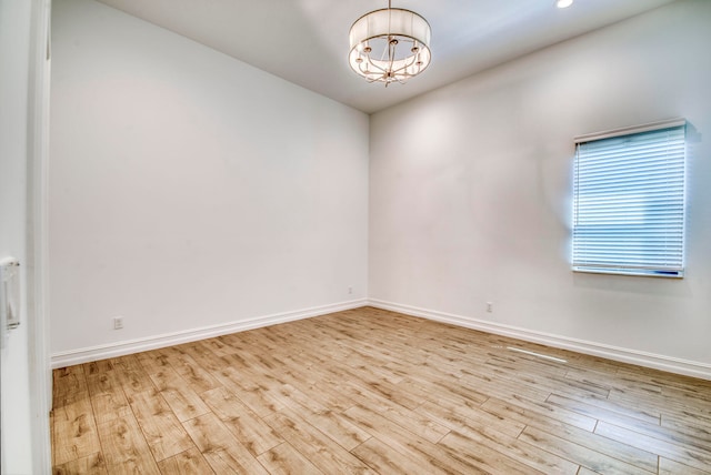 spare room featuring an inviting chandelier and light hardwood / wood-style floors