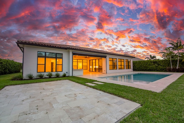 back house at dusk with a fenced in pool, a yard, and a patio area