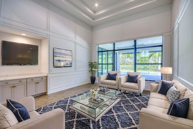 living room with light wood-type flooring, a raised ceiling, and a high ceiling