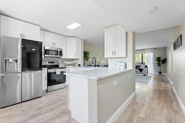 kitchen featuring kitchen peninsula, white cabinets, stainless steel appliances, and a textured ceiling