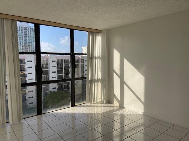 empty room with a wall of windows, light tile patterned flooring, and a textured ceiling