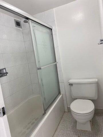 bathroom featuring toilet, tile patterned floors, and shower / bath combination with glass door