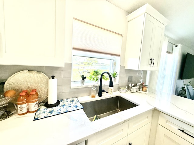 kitchen with white cabinetry, sink, light stone counters, and decorative backsplash