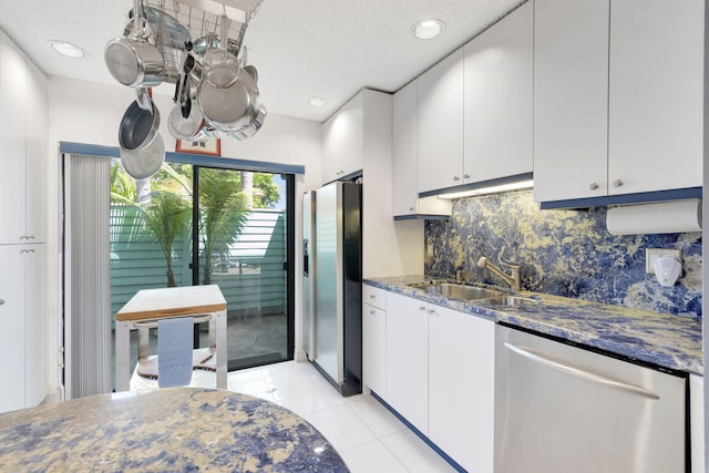kitchen featuring backsplash, a sink, light tile patterned floors, stainless steel appliances, and white cabinetry