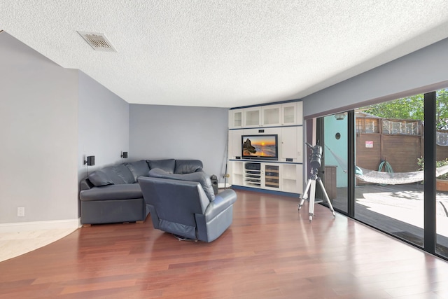 living room with visible vents, baseboards, a textured ceiling, and wood finished floors