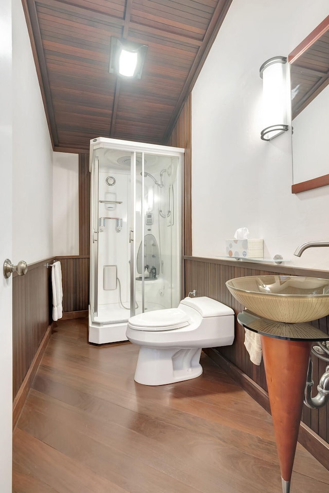 bathroom featuring wainscoting, a shower stall, wood finished floors, toilet, and wooden walls