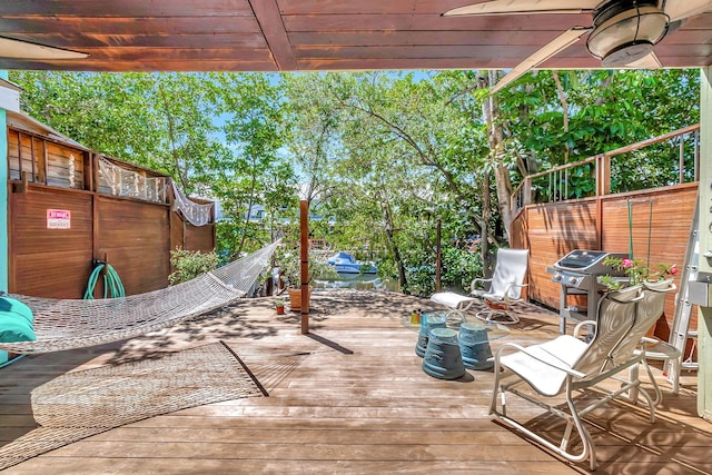 wooden terrace with area for grilling, fence, and a ceiling fan