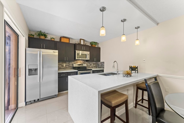 kitchen with appliances with stainless steel finishes, sink, kitchen peninsula, a kitchen breakfast bar, and decorative light fixtures