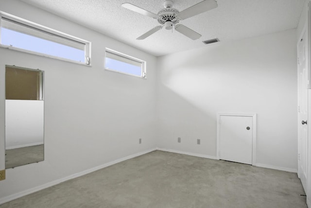carpeted spare room featuring a textured ceiling, visible vents, baseboards, and ceiling fan