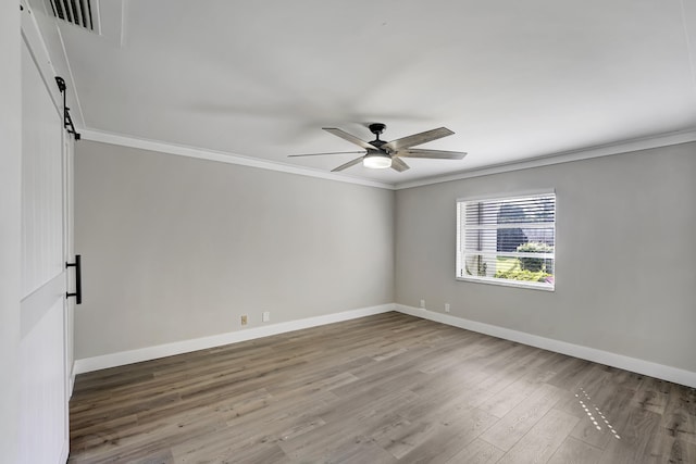 empty room featuring crown molding, a barn door, wood-type flooring, and ceiling fan