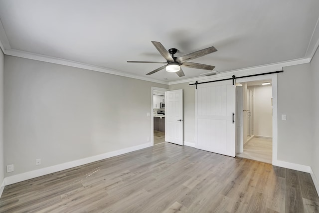 unfurnished bedroom with light hardwood / wood-style floors, ornamental molding, a barn door, and ceiling fan