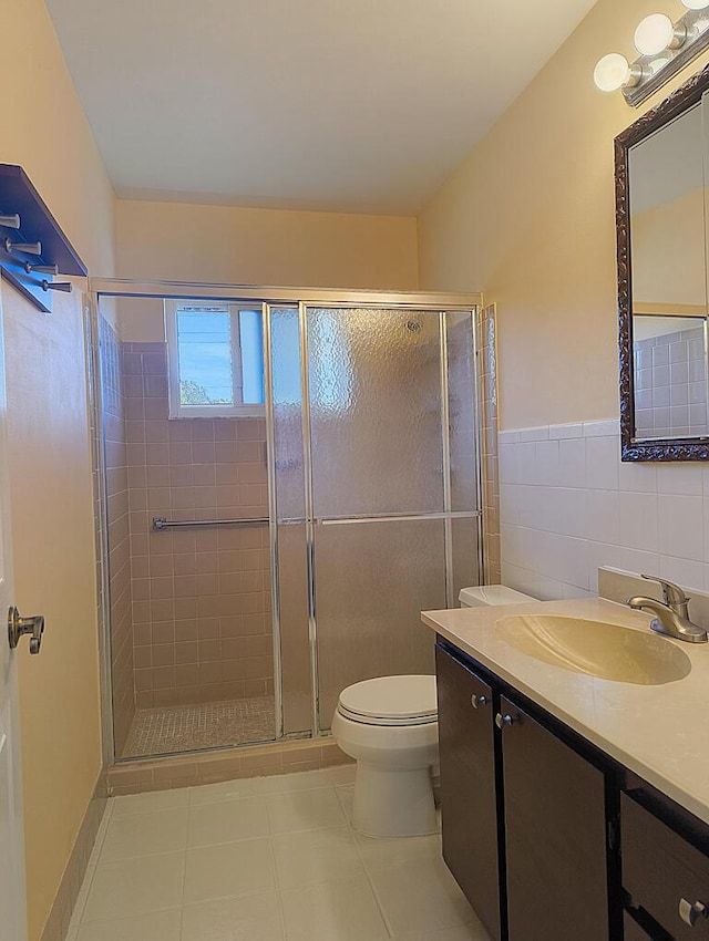 bathroom with a shower with door, tile walls, vanity, tile patterned floors, and toilet