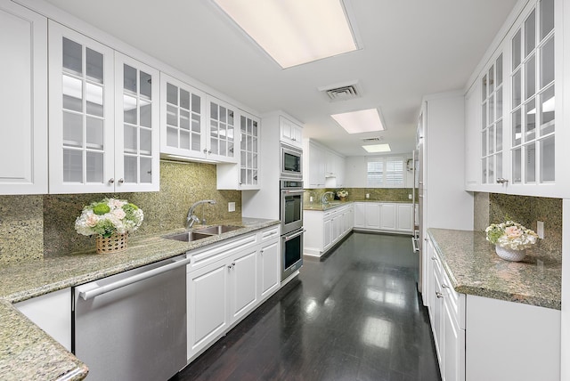 kitchen with sink, dark wood-type flooring, light stone counters, white cabinets, and appliances with stainless steel finishes