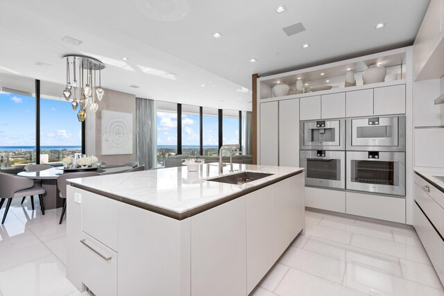 kitchen featuring white cabinetry, double oven, sink, and a kitchen island with sink