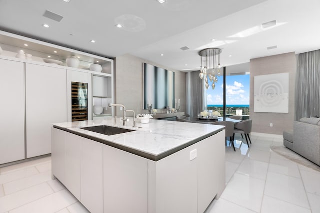 kitchen with a center island with sink, sink, pendant lighting, white cabinets, and light stone counters