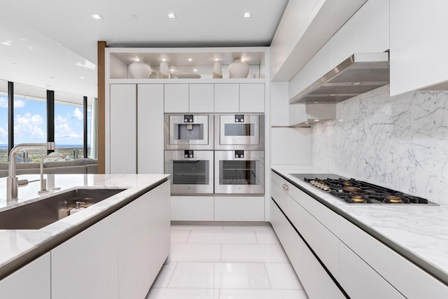 kitchen featuring tasteful backsplash, wall chimney range hood, sink, appliances with stainless steel finishes, and white cabinetry