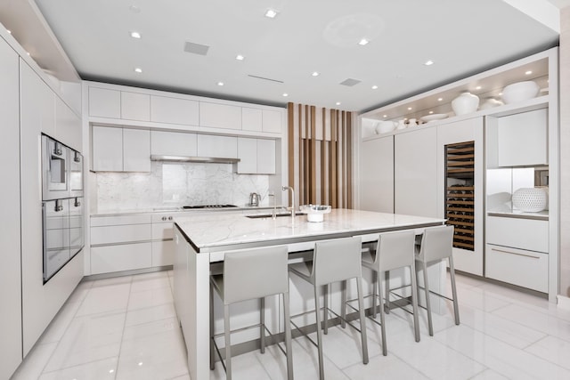 kitchen with beverage cooler, an island with sink, a kitchen breakfast bar, and white cabinets