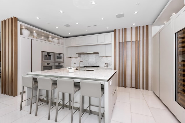 kitchen featuring white cabinets, a spacious island, a kitchen breakfast bar, light stone countertops, and sink