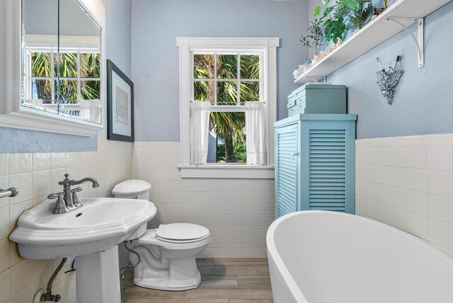 323 Dyer Rd, West Palm Beach, FL 33405 - full bathroom featuring tile walls, a freestanding bath, wood finished floors, toilet, and a wainscoted wall