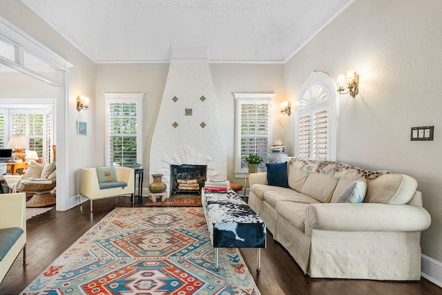 living room featuring dark wood-type flooring, ornamental molding, and a stone fireplace