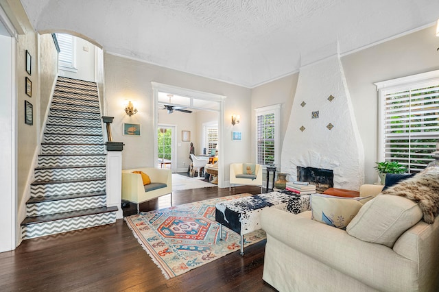 living room with ceiling fan, a fireplace, crown molding, dark wood-type flooring, and a textured ceiling