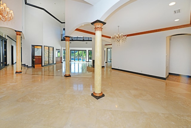 empty room featuring a notable chandelier, a high ceiling, crown molding, and decorative columns