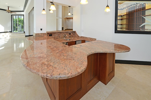 kitchen with kitchen peninsula, light stone countertops, hanging light fixtures, and ceiling fan