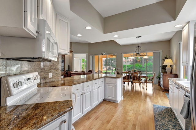 kitchen with a peninsula, white electric range, white cabinets, hanging light fixtures, and dark stone counters