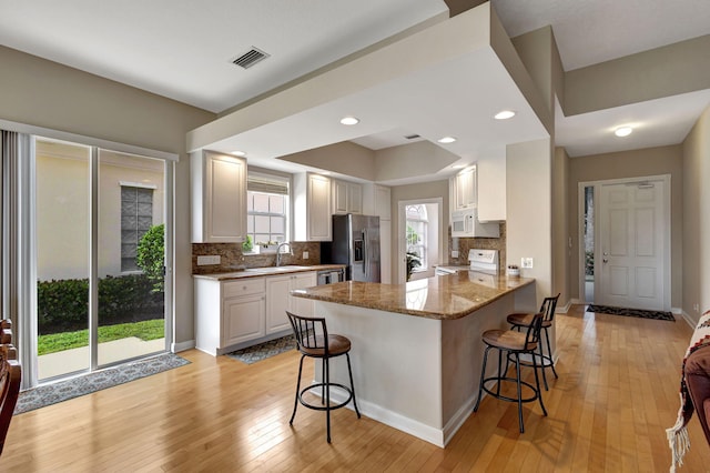 kitchen with stone counters, kitchen peninsula, a kitchen bar, white cabinets, and appliances with stainless steel finishes