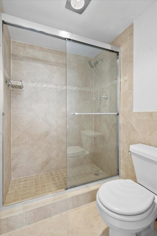 bathroom with an enclosed shower, tile patterned flooring, toilet, and tile walls