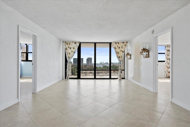 tiled spare room with floor to ceiling windows, plenty of natural light, and a textured ceiling