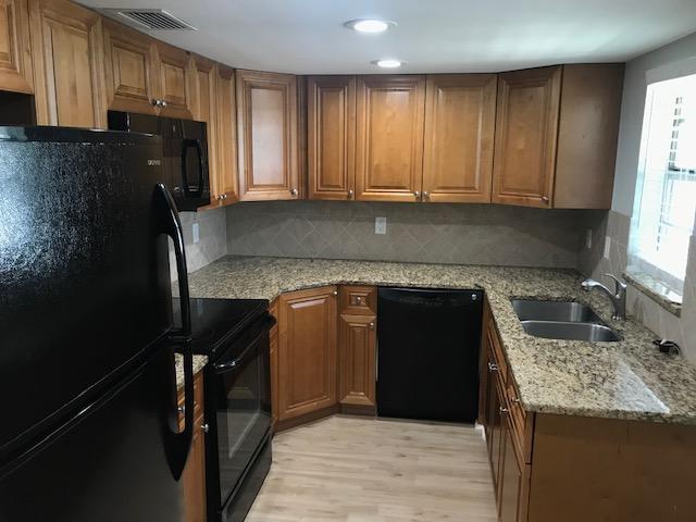 kitchen with tasteful backsplash, light stone countertops, black appliances, sink, and light hardwood / wood-style floors